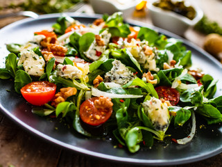 Fresh salad - blue cheese, cherry tomatoes, vegetables and walnuts on wooden background
