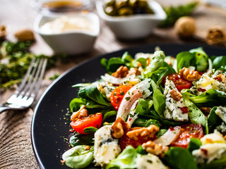 Fresh salad - blue cheese, cherry tomatoes, vegetables and walnuts on wooden background
