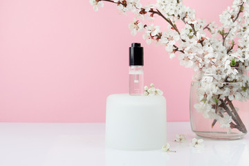 Bottle of hyaluronic acid, cosmetic serum or essential oil with white flowers on pink background. Beauty concept