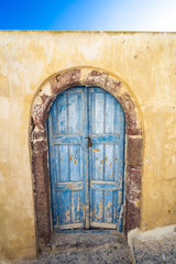 Fototapeta na wymiar old blue wooden door and yellow wall in Oia street, Architecture, picturesque, Santorini island, Cyclades, Greece