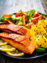 Fried salmon steak with potatoes and vegetables on wooden table
