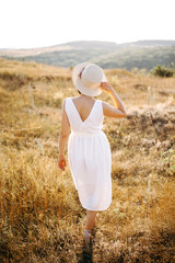 Beautiful girl with hat walks in the mountains and enjoys the sunset. Back view