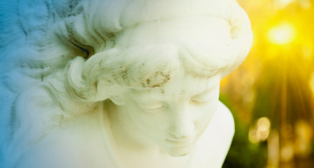 Fragment of ancient stone statue of beautiful white guardian angel in sun rays. Horizontal image.
