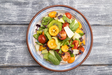 Vegetarian salad of pac choi cabbage, kiwi, tomatoes, kumquat, microgreen sprouts on gray wooden background. Top view.
