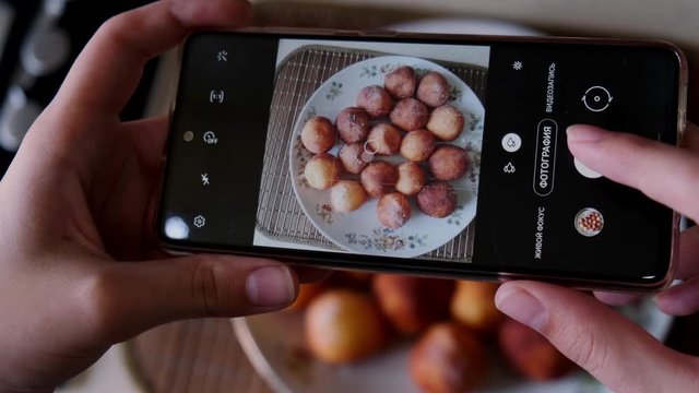 Housewife woman food blogger makes photo of delicious homemade donut cheese balls on a plate by phone. Hands closeup.