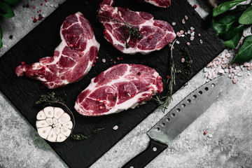Pork neck on a black board with herbs