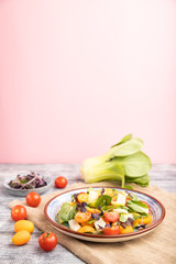 Vegetarian salad of pac choi cabbage, kiwi, tomatoes, kumquat, microgreen sprouts on gray wooden background. Side view, selective focus, copy space.