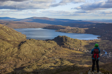 Fototapeta premium a mountaineer remains standing observing the lake of sanabria with beautiful clouds in the sky and a calm and beautiful scenary. Lake of Sanabria