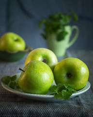Green apples with sprigs of mint on a green plate, in the background a green mug
