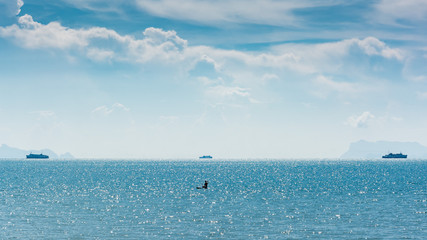 Man on a paddle board taking a selfie with three ferries in the background on Koh Samui, Thailand.
