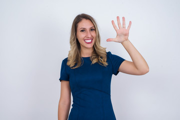 Young woman standing against gray wall showing and pointing up with fingers number five while smiling confident and happy.