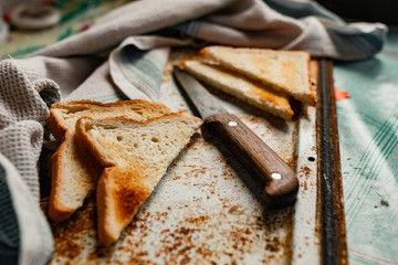 Triangular slices of toasted white bread with a soft texture inside and a crisp crust on the outside on a rusty metal background, next to an old knife with a wooden handle