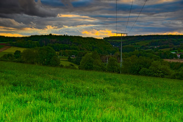 Dramatic sunset over Germany

A picturesque area in Germany just before sunset in the golden hour. A lonely electricity pylon stands on a meadow. Behind it are several small groves