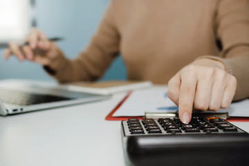 businesswoman working about finance on calculator with laptop computer and document report on desk...