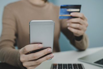 young woman entering security code with digital mobile phone and paying with mock up credit card and calculator on desk at home, shopping online, electronic pay, digital marketing, technology concept