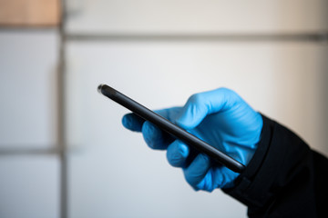 Man wearing PPE protective blue gloves using a touchscreen smartphone during Coronavirus Covid-19 outbreak. Concept for technology during pandemic