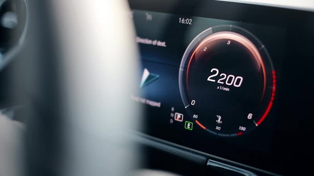 Close up footage of the digital display of a modern car, with a revving tachometer. 