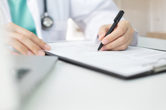 Asian Woman Doctor With Green Cloth And Lab Coat Working And Taking Note Information Of Patient In Checklist Paper On Clipboard In Medical Room Of Hospital. Health Care