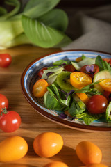 Vegetarian salad of pac choi cabbage, kiwi, tomatoes, kumquat, microgreen sprouts on a wooden background. Side view, close up, hard light, selective focus.