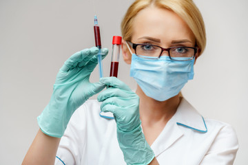 Doctor or woman nurse wearing protective mask holding syringe and blood test tube