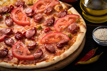 pizza with bavarian sausages, tomato and chili pepper on dark background