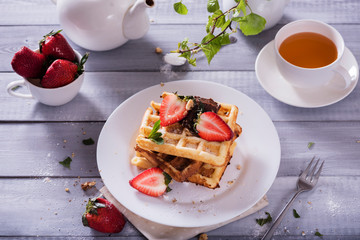 Plate of Belgian waffles with chocolate sauce and fresh  strawberries on white background. Delicious sweet dessert with cup of  tea.