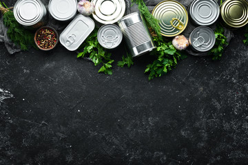 Set of tin cans with food on black stone background. Food stocks. Top view. Free space for your...