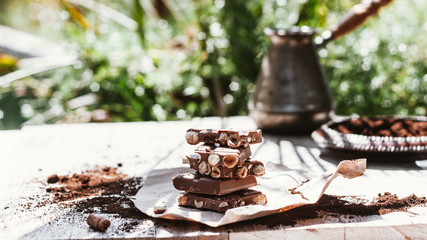 Hazelnut and almond milk chocolate pieces tower is recycled paper on wooden table with green nature blurred background