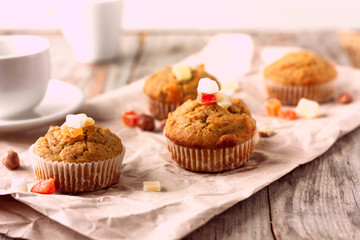 Freshly baked banana muffins with candied fruit lay on recycled paper on wooden table. Morning breakfast concept