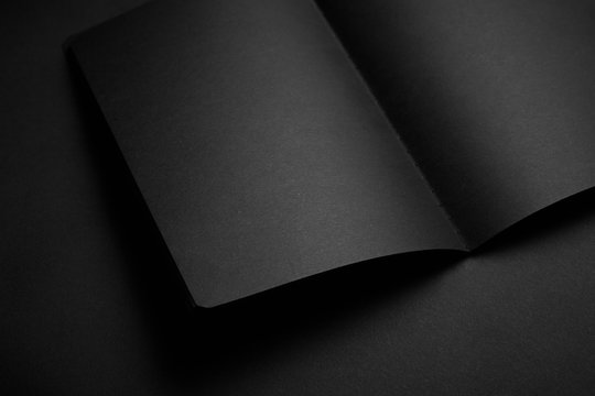 Blank black notebook on a black table, mockup photo. Blank black cover template with copy space for design. Black on black, minimal design concept.
