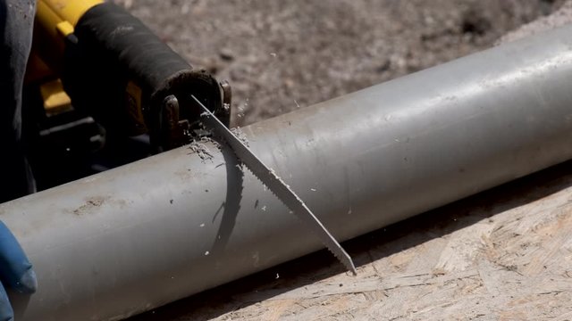 Plumber man in rubber gloves, cuts the plastic sewer pipe, electric saber saw. Close-up.