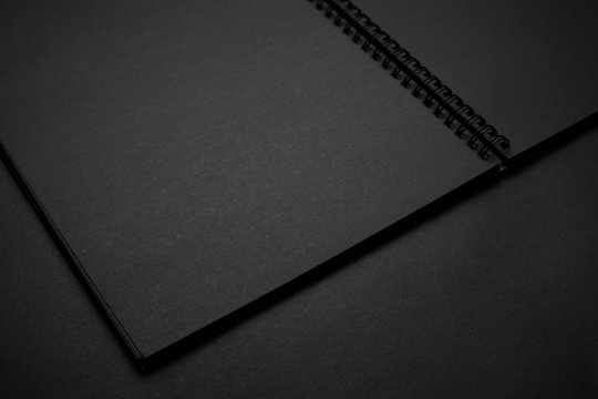 Blank black notebook on a black table, mockup photo. Blank black cover template with copy space for design. Black on black, minimal design concept.