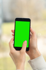 female hand holds a smartphone with a green screen, chromakey. close up on a light background
