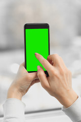 female hand holds a smartphone with a green screen, chromakey. close up on a light background. vertical