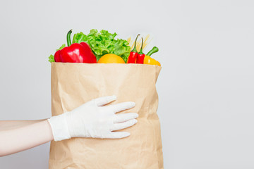 Female hands in medical gloves hold a paper bag with food, vegetables, pepper, chili , fresh herbs isolated over white, gray background, quarantine, coronavirus, safe eco food shopping delivery