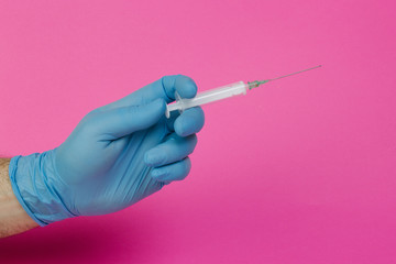 hand with latex gloves and syringe on pink background