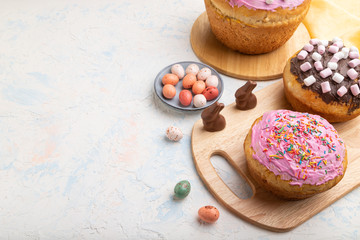 Homemade glazed and decorated easter pies with chocolate eggs and rabbits on a white concrete background. Side view, copy space.