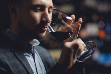 Sommelier man holds glass with red wine in restaurant, tests aroma and color