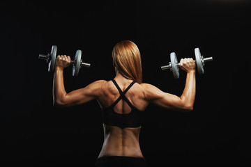 Attractive fitness model with dumbbells posing on a dark background in sportswear. Fitness motivation, beautiful body, achieving goals, blood sweat tears, overcoming oneself.