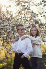 Fototapeta premium Two little Caucasian children wolk in the park with each other. Brother and sister spend time together.older brother help his younger sister with homework. Stylish clothes,cool glasses and happy faces