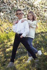 Fototapeta premium Two little Caucasian children wolk in the park with each other. Brother and sister spend time together.older brother help his younger sister with homework. Stylish clothes,cool glasses and happy faces