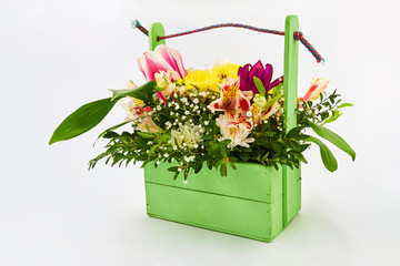 Multi-colored flowers in a green wooden basket on a white background