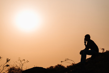 Fototapeta na wymiar Silhouette of an Indian man sitting in front of the sunset at Wankaner, Gujarat, India