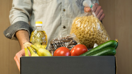 A man puts macaroni in a donation box. Donations to the needy and the starving during coronavirus. Macaroni, crackers, oil, bread, cucumbers, bananas, tomatoes.