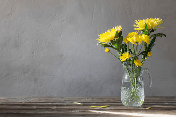 yellow chrysanthemum in glass  jug on background old wall