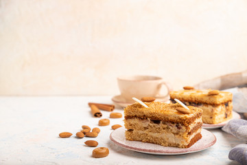 Honey cake with milk cream, caramel, almonds and a cup of coffee on a white concrete background. Side view, copy space, selective focus.
