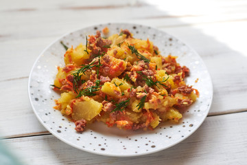 Baked potatoes with minced meat, onions and carrots baked on a plate on a light wooden background.