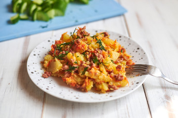 Baked potatoes with minced meat, onions and carrots baked on a plate on a light wooden background.