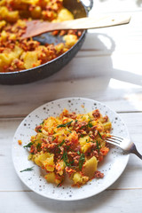 Baked potatoes with minced meat, onions and carrots baked on a plate on a light wooden background.