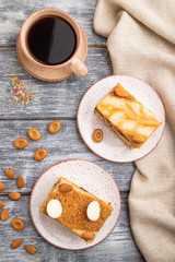 Honey cake with milk cream, caramel, almonds and a cup of coffee on a gray wooden background. Top view, close up.
